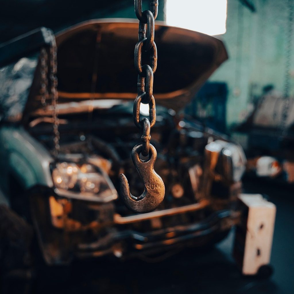 Engine hoist chain hanging over a car with its hood open in a repair bay