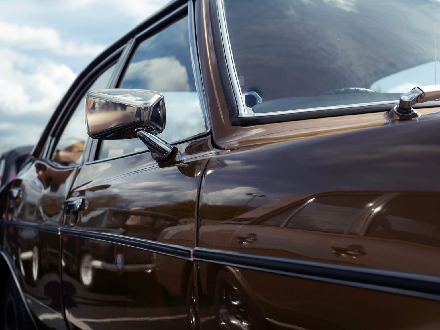 Side of a dark sedan with its door mirror and window trim in daylight